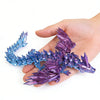 A hand holds a purple and blue 3D printed magic dragon ornament made of crystals.
