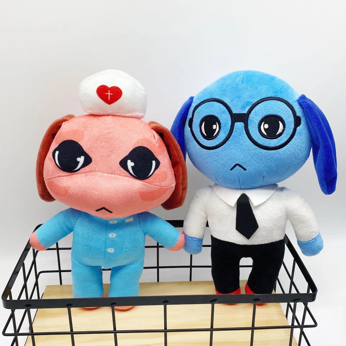 A plush toy of a blue dog with large glasses and a white shirt, standing next to a pink animal hospital plush.