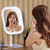 A woman uses an LED touch-sensitive vanity mirror with a ring light to apply makeup.