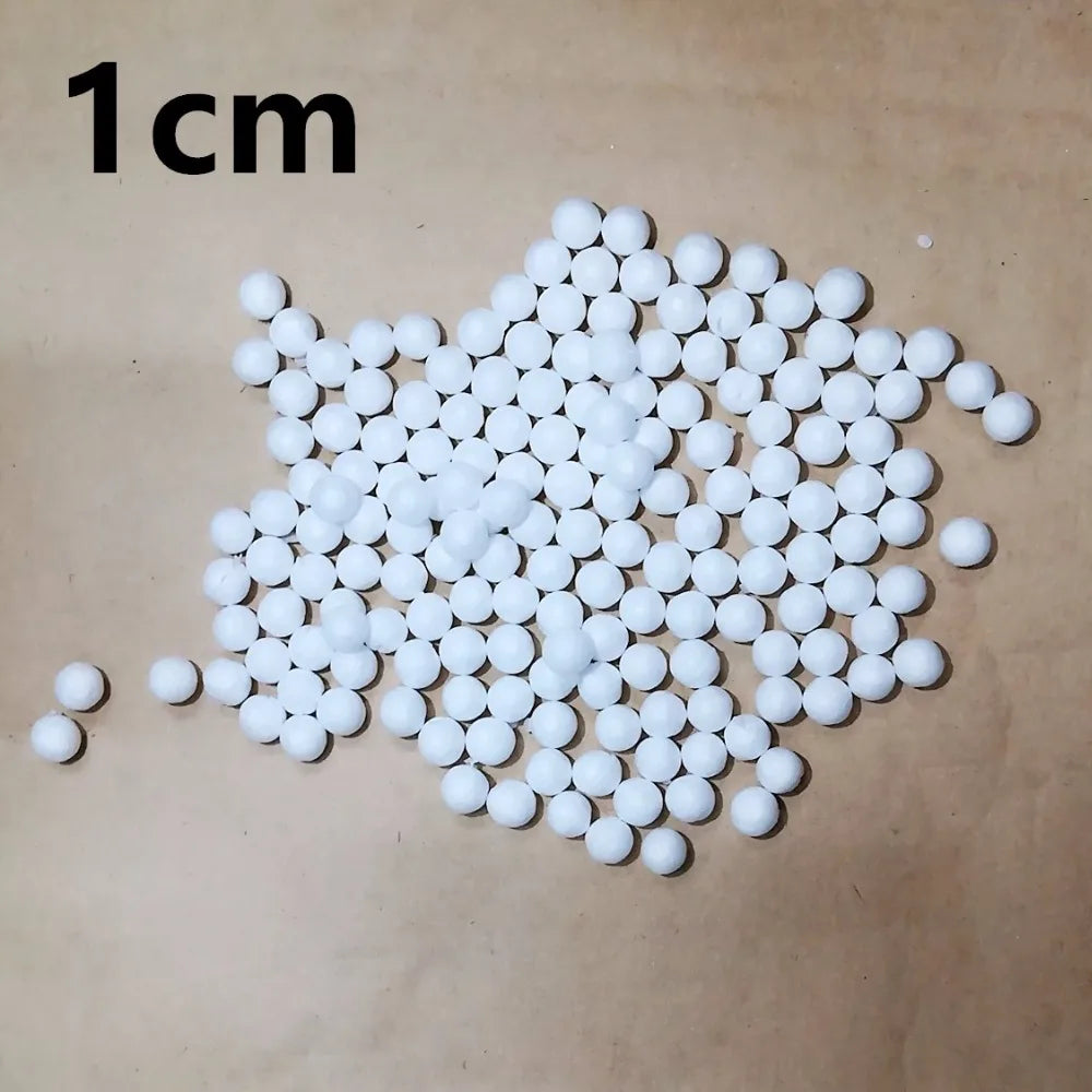 A scattering of small white polystyrene foam balls on a brown surface, with a 1cm scale marker.