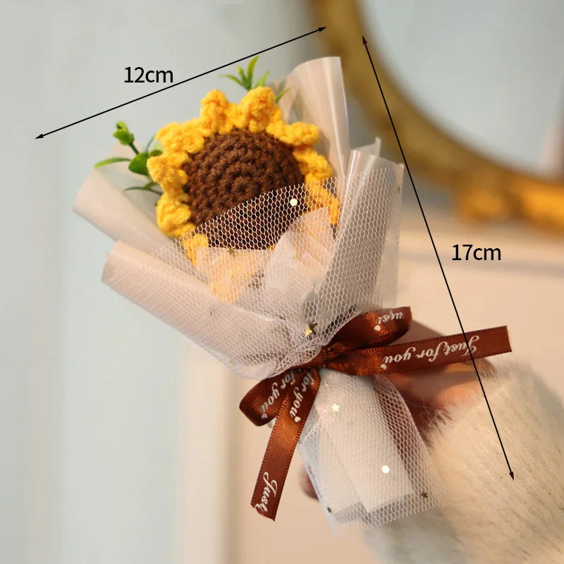 A bouquet of handmade crochet flowers featuring a yellow flower with a brown center, wrapped in white paper and tied with a b