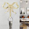 A brass elegant bowknot wall hook with a loop for home organization mounted on a light gray wall.