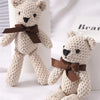 A light beige crocheted stuffed bear toy with a brown bow, displayed next to a gift ornament.