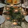 Clear glass tealight candle holders arranged on a lace tablecloth with green foliage for table centerpieces