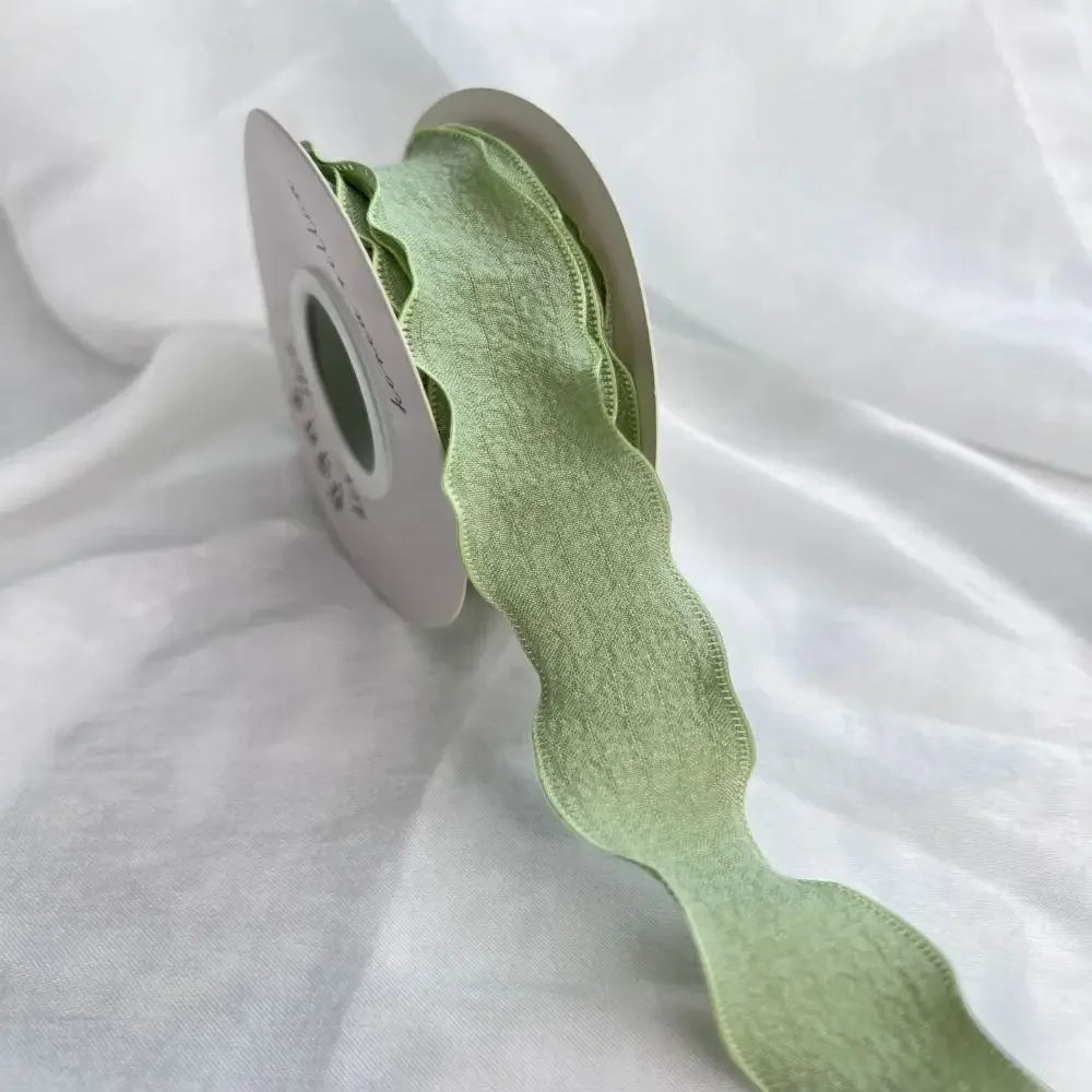 A light green decorative fishtail yarn ribbon is shown rolled on a pale gray card.