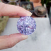 A hand holds a round, faceted purple crystal ice crack ball used as water fountain decor.