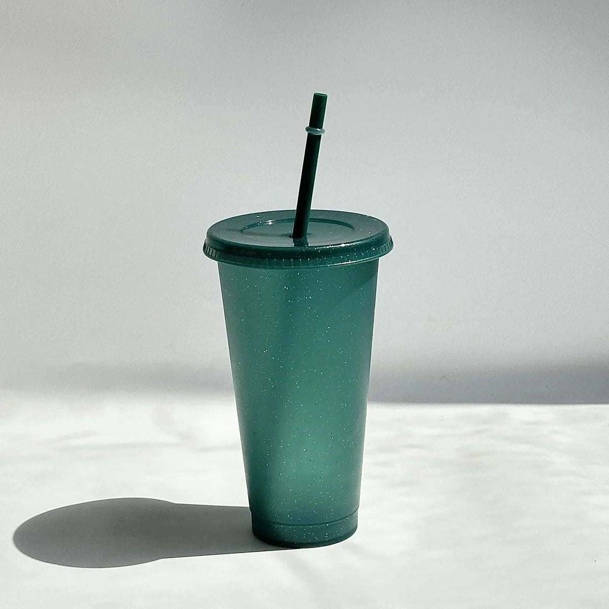 A green glitter party cup with a black straw is shown against a white background.