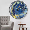 A minimalist round wall clock with a blue and yellow abstract design on a white background.
