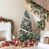 A flocked artificial Christmas tree decorated with ornaments and ribbon, displayed in a white room setting.