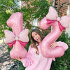 A woman holding a large pink number balloon decoration set outdoors.
