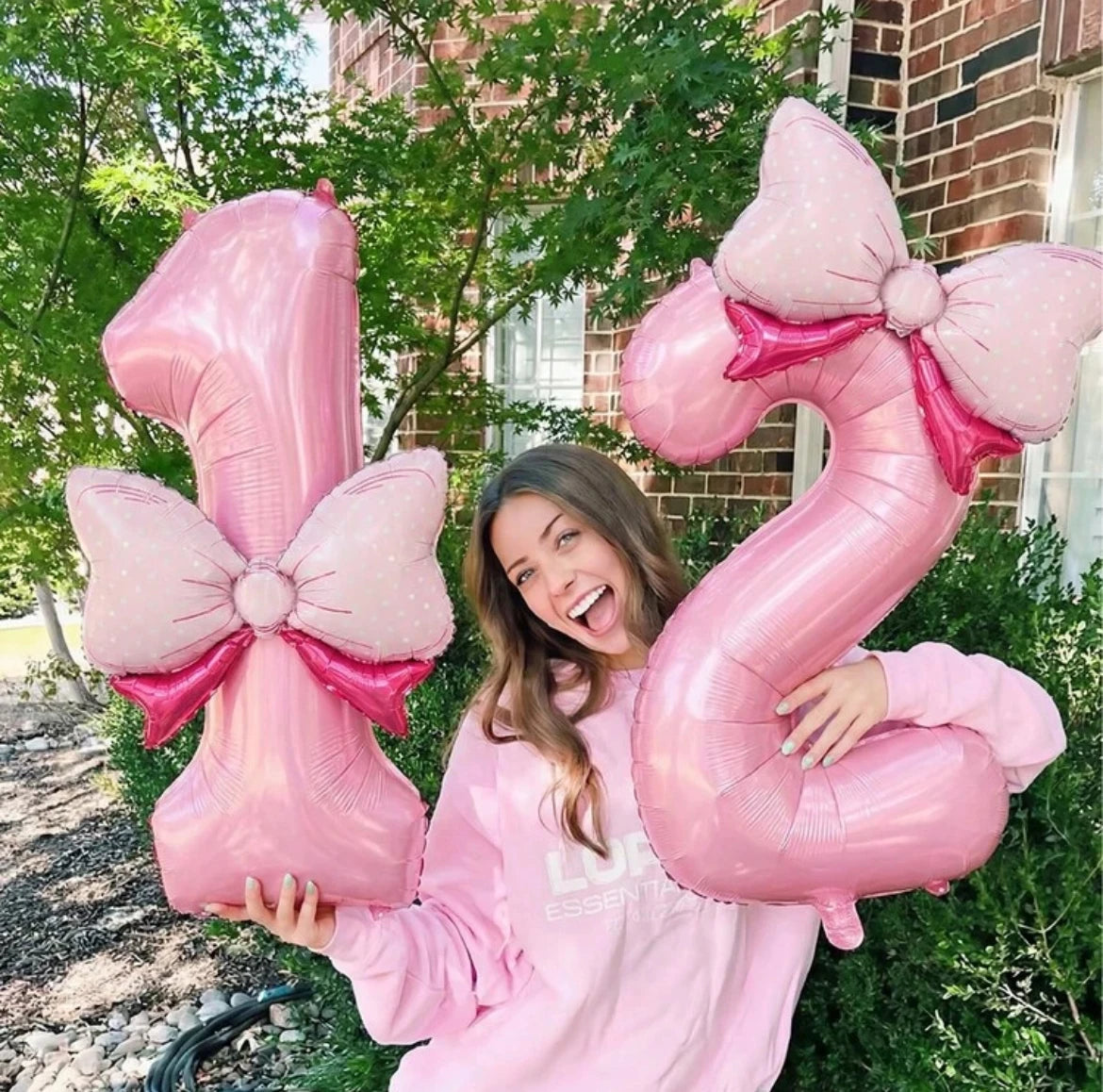 A woman holding a large pink number balloon decoration set outdoors.