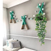Hanging artificial plant wall decor featuring green foliage and white decorative accents on a gray wall.