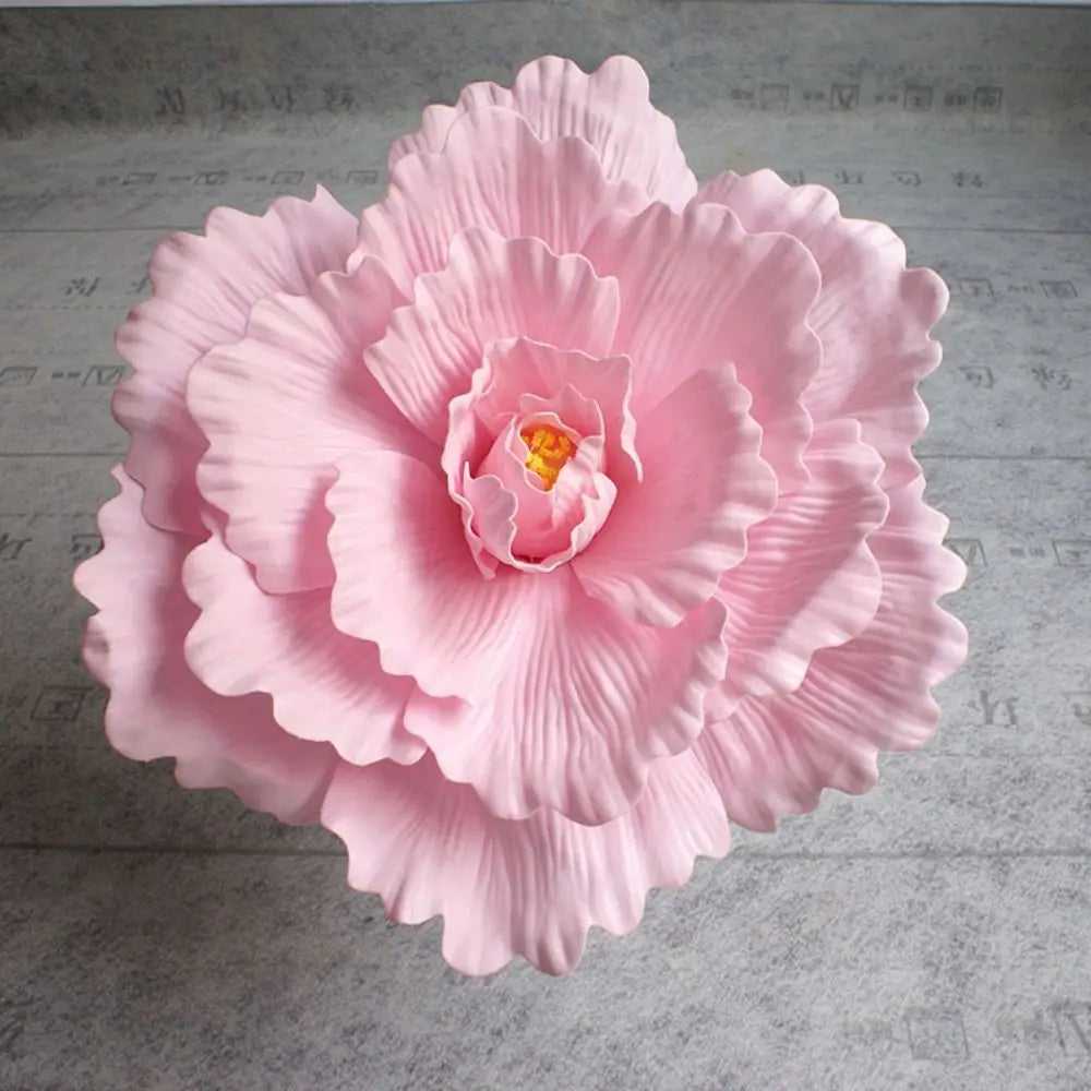 A large, pink silk foam rose flower with layered petals and a yellow center.