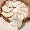 A collection of wooden baby milestone cards showing numbers 10 through 12 months with pink ribbon details.