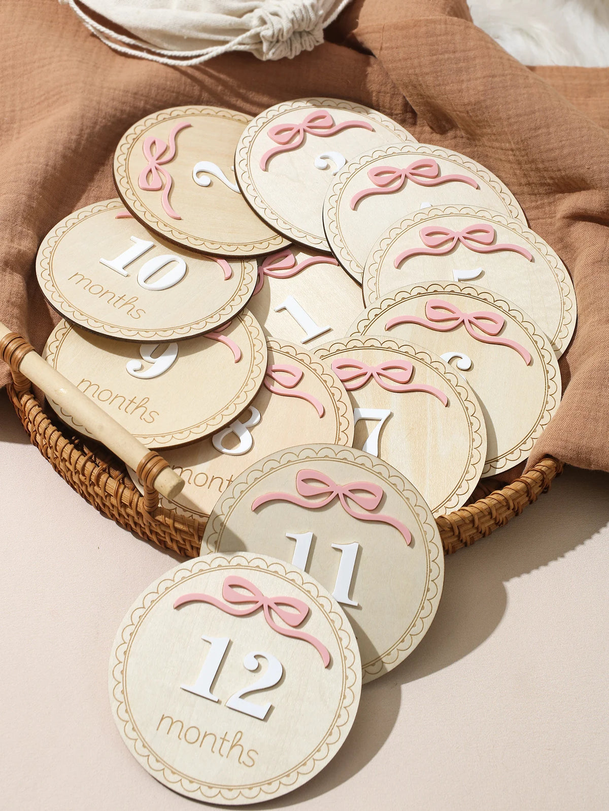 A collection of wooden baby milestone cards showing numbers 10 through 12 months with pink ribbon details.