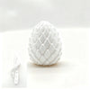 A white, textured dragon egg fidget toy is shown on a white surface with a smaller version next to it.