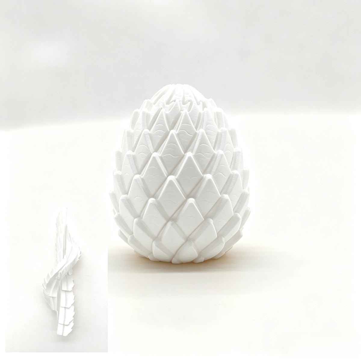 A white, textured dragon egg fidget toy is shown on a white surface with a smaller version next to it.