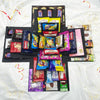 A black gift box is filled with various colorful party snacks and candies arranged in a cross shape.