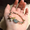 A hand holds a raw aquamarine macrame bracelet featuring a rose accent and small blue stones.