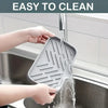 Hands are rinsing a silicone faucet splash guard and drying mat under a kitchen faucet.
