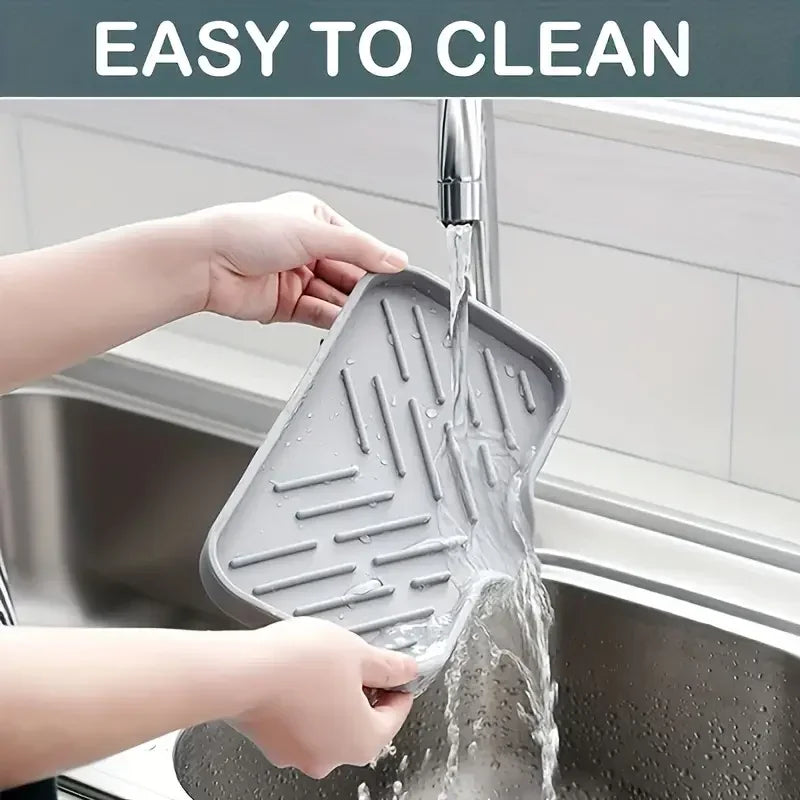 Hands are rinsing a silicone faucet splash guard and drying mat under a kitchen faucet.