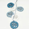 A set of twelve wooden ocean ornaments in shades of blue and white, shaped like shells, scallops, and starfish.