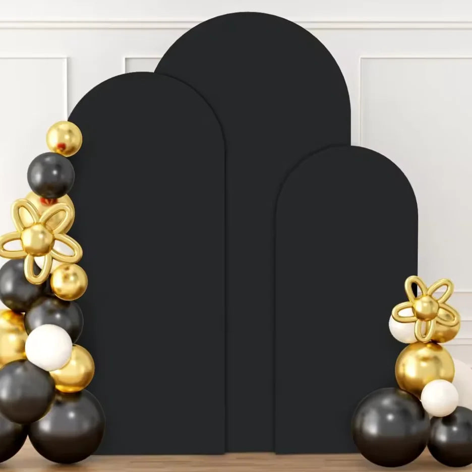 A set of three black spandex wedding arch covers with gold and white spherical decorations displayed against a white wall.