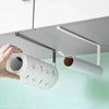 A hand holds a roll of white paper with orange and green designs, positioned under a metal holder for kitchen or bathroom use