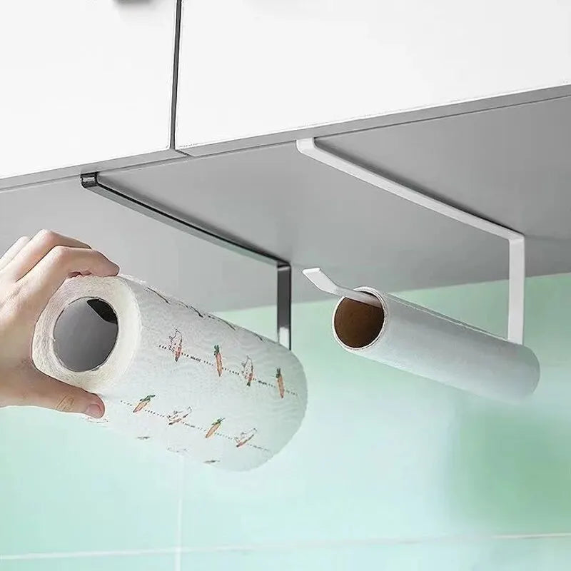 A hand holds a roll of white paper with orange and green designs, positioned under a metal holder for kitchen or bathroom use