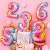 A collection of rose gold and silver gradient foil balloons shaped like the numbers 2, 3, 5, and 6 arranged on a pink backgro