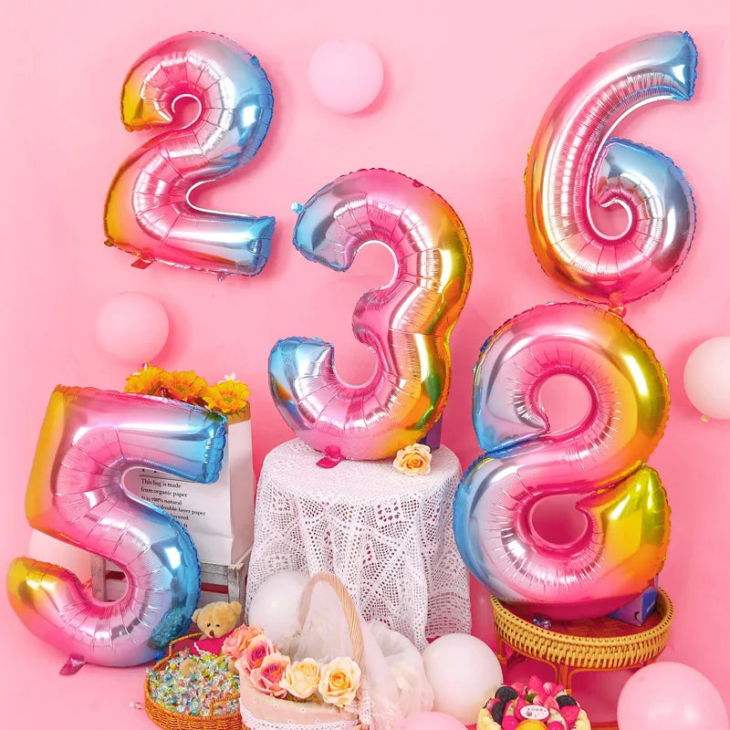 A collection of rose gold and silver gradient foil balloons shaped like the numbers 2, 3, 5, and 6 arranged on a pink backgro