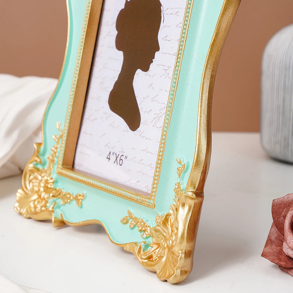 A gold-framed photo frame with a light mint green border and a dark silhouette of a woman on a white background.