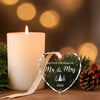 A glowing candle next to a heart-shaped crystal ornament engraved with Our First Christmas As Mr & Mrs 2026