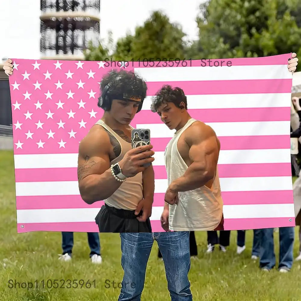 Two muscular men stand holding a pink and white American flag banner with stars and stripes.