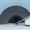 Black titanium alloy folding hand fan with a repeating wave pattern displayed on a light blue background.