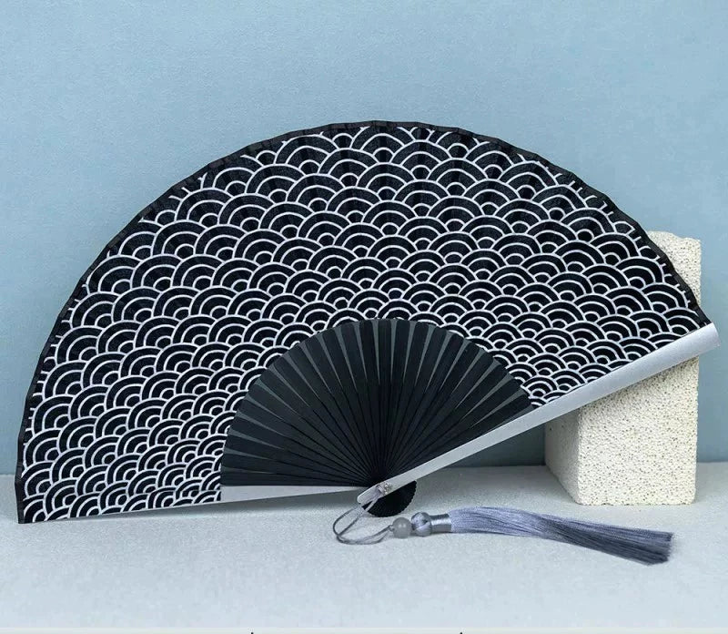 Black titanium alloy folding hand fan with a repeating wave pattern displayed on a light blue background.