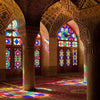 Interior view of an Islamic mosque with arched windows and columns, featuring colorful stained glass and patterned rugs.