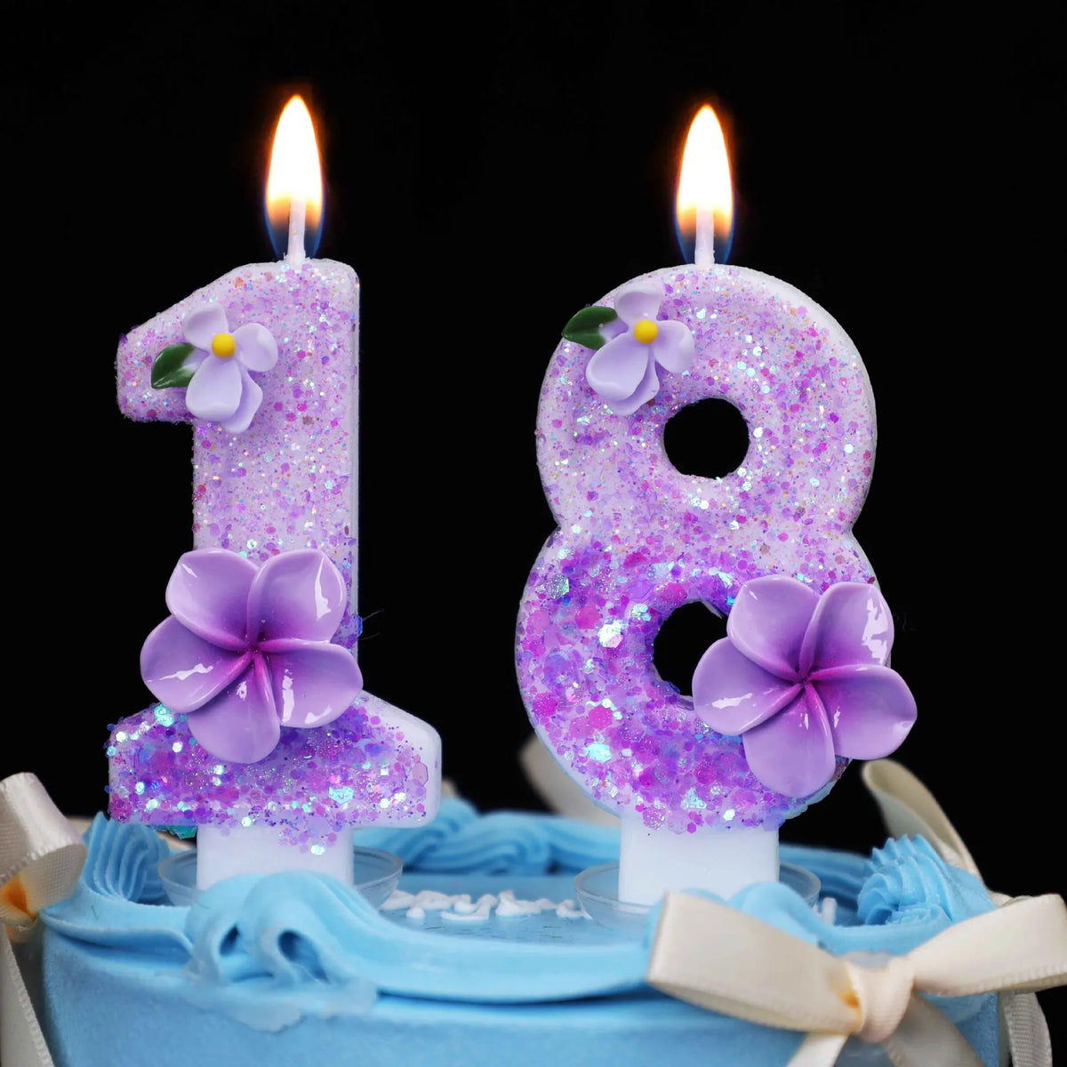 Two purple glitter flower number candles, 1 and 8, on a blue cake.