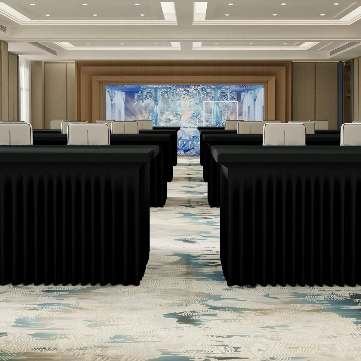 A long hall with rows of black tables draped in elastic fitted spandex tablecloths, leading toward a brightly lit blue floral