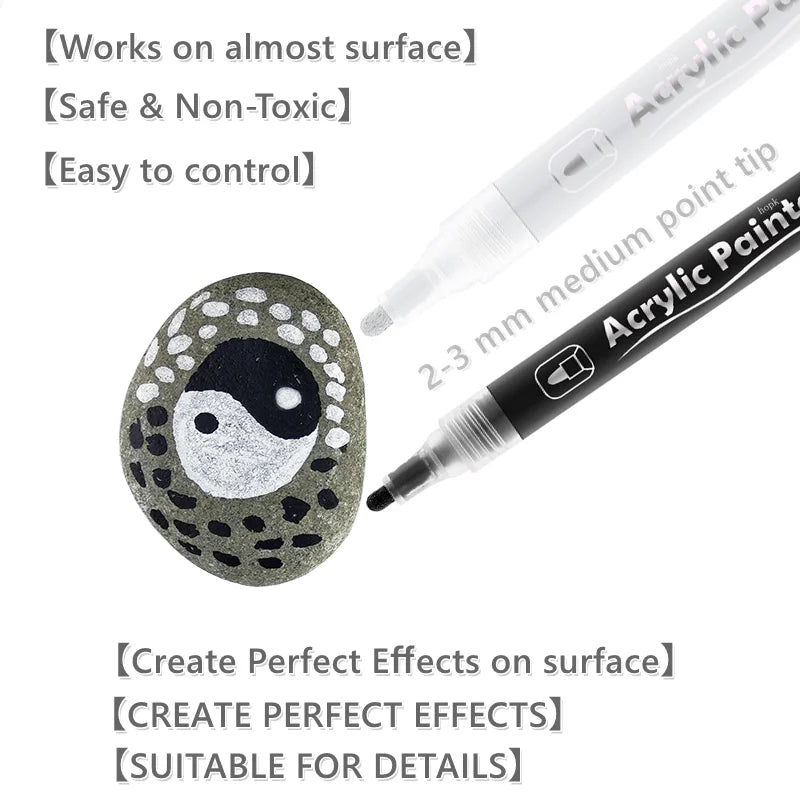 A black acrylic paint pen with a fine tip is shown next to a round, dark gray stone decorated with white dots and a Yin-Yang 