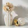 Gold-plated ceramic vase with dried grasses and a smaller white vase on a white shelf