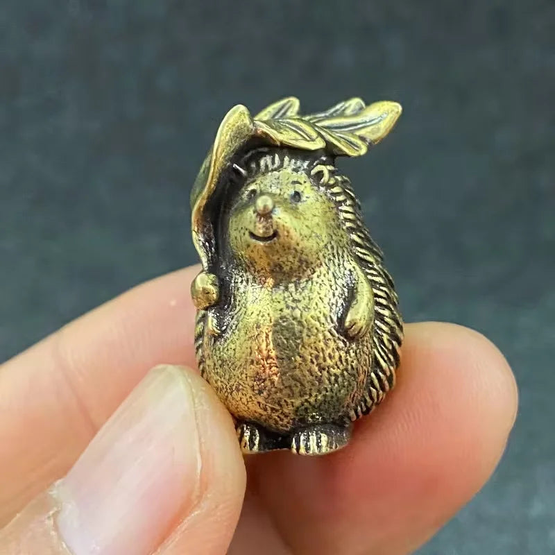 A small brass figurine of a hedgehog with leaves and flowers, held in a person's hand.