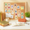 A framed display of cute animal vinyl stickers on a cork board next to a calendar and notebooks.