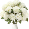 A bouquet of white artificial chrysanthemum flower balls with green leaves in a white vase.