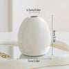 A white ceramic mini vase with a smooth, rounded shape is shown on a light surface.