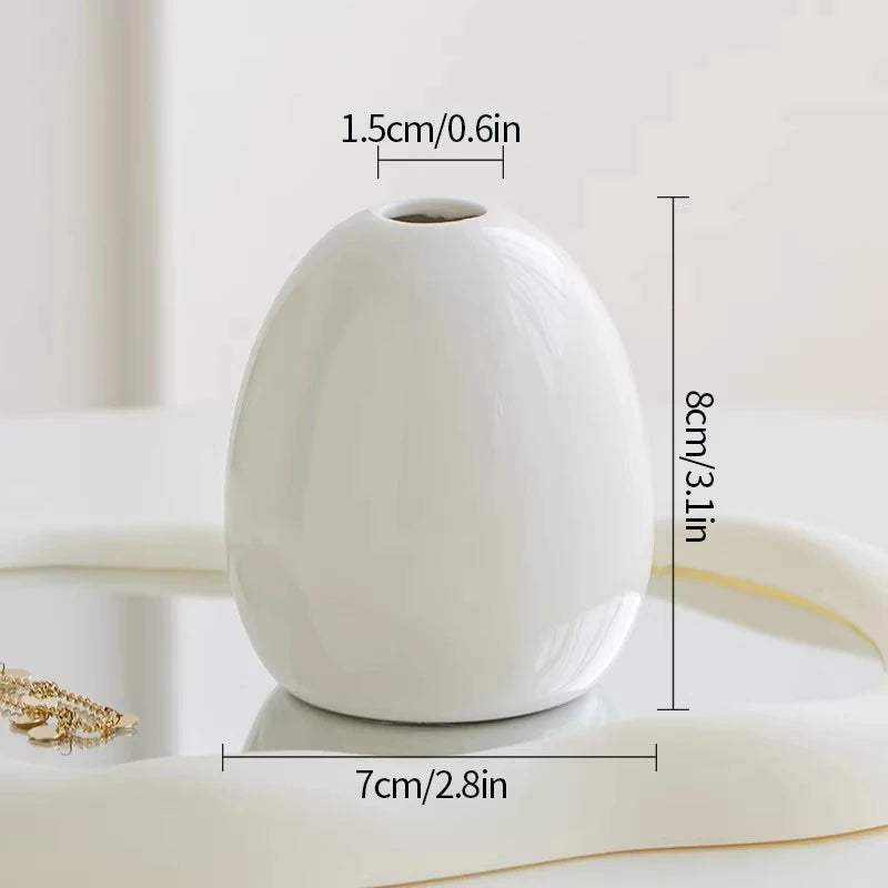 A white ceramic mini vase with a smooth, rounded shape is shown on a light surface.