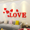 Red acrylic heart wall stickers spelling the word LOVE displayed on a white wall above a gray sofa.