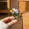A hand holds a small glass vase filled with colorful handcrafted mini flowers.