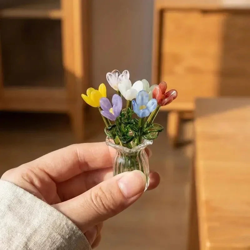 A hand holds a small glass vase filled with colorful handcrafted mini flowers.