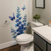 A white toilet features a blue flower and butterfly wall decal decoration on the surrounding wall.